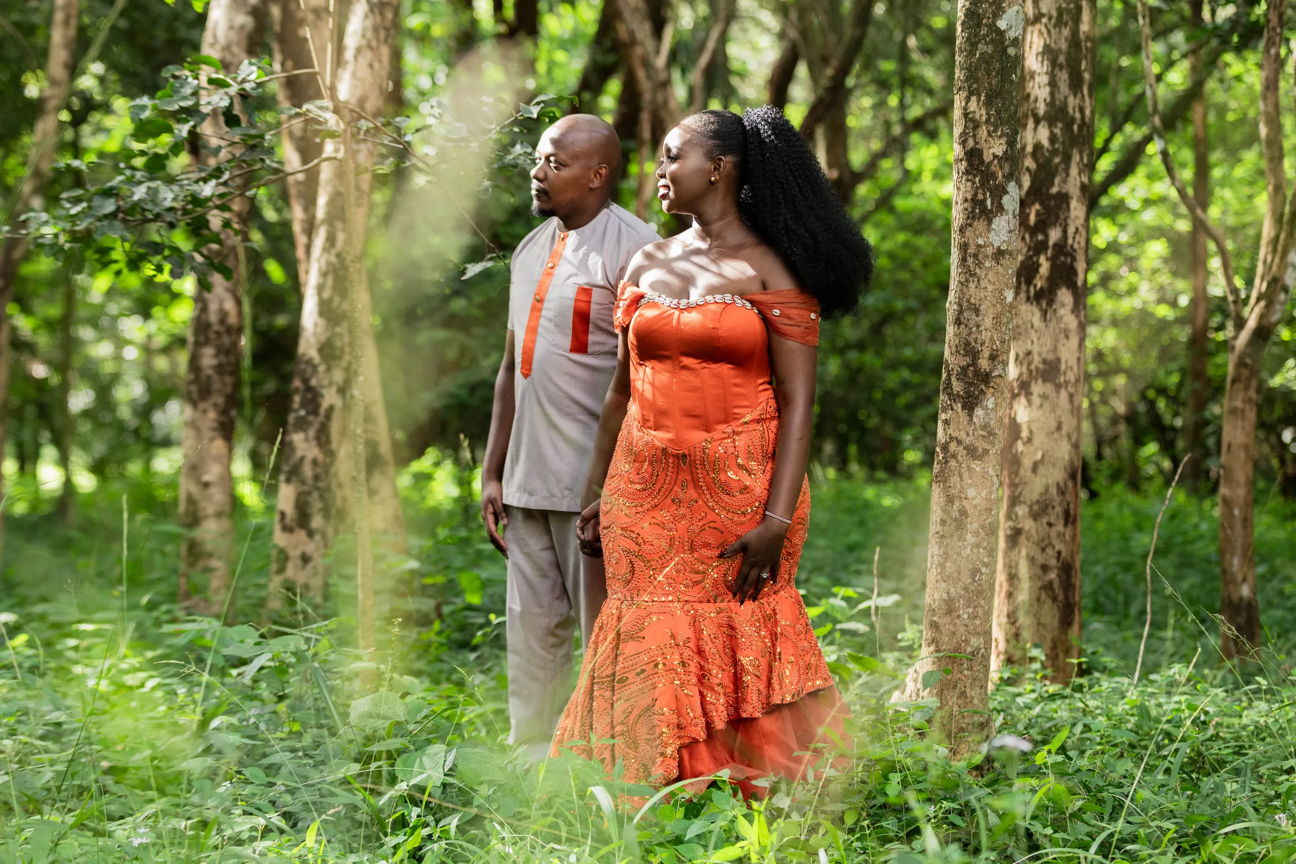 Couple among sunlit trees in their orange and grey outfits