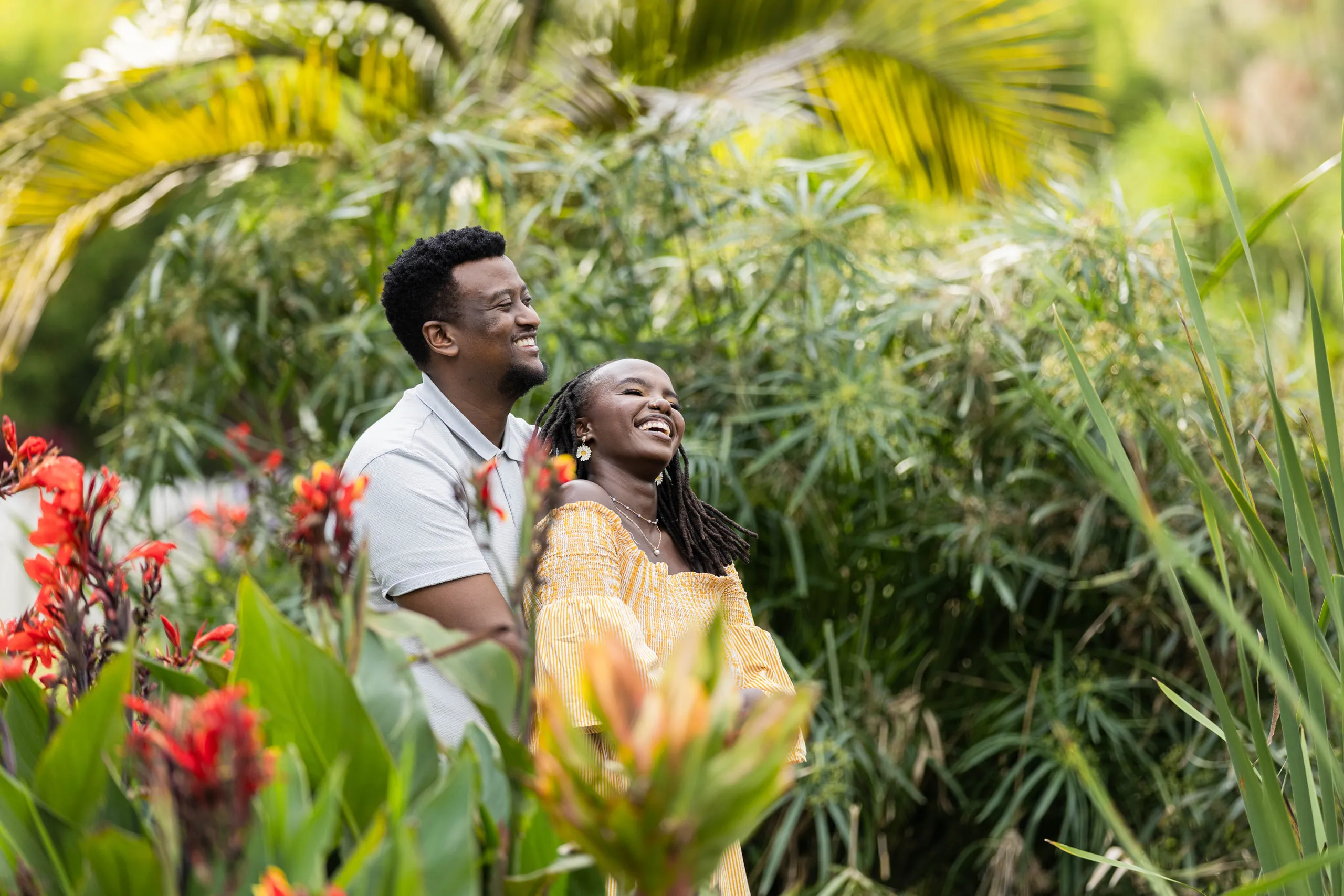 Couple laughing among red flowers and palms, she in yellow
