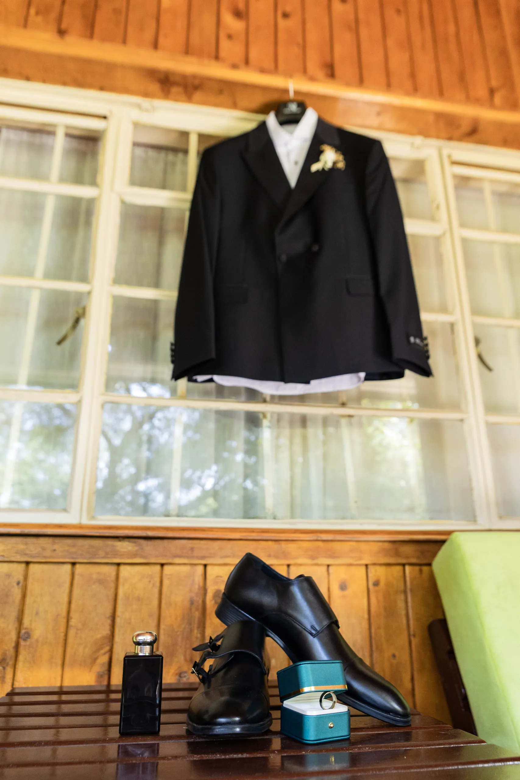 Groom's black suit hanging in a window above his shoes and the ring box