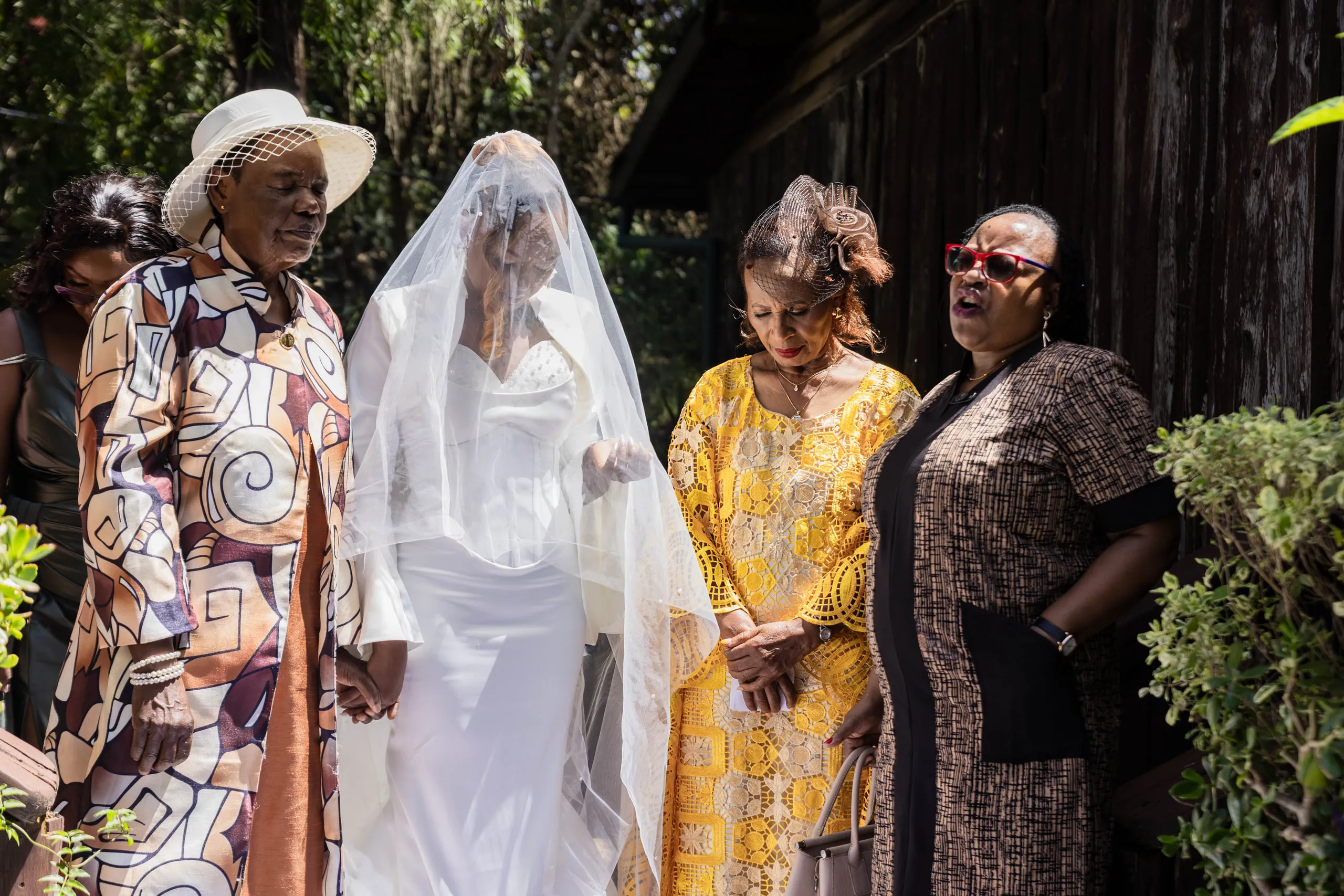 Veiled bride led out by an elder in a patterned suit, family beside her