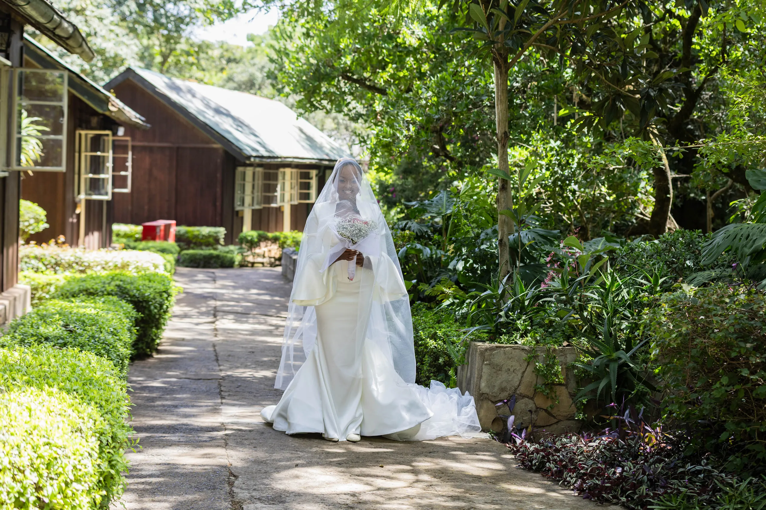 Veiled bride on a garden path beside wooden cottages