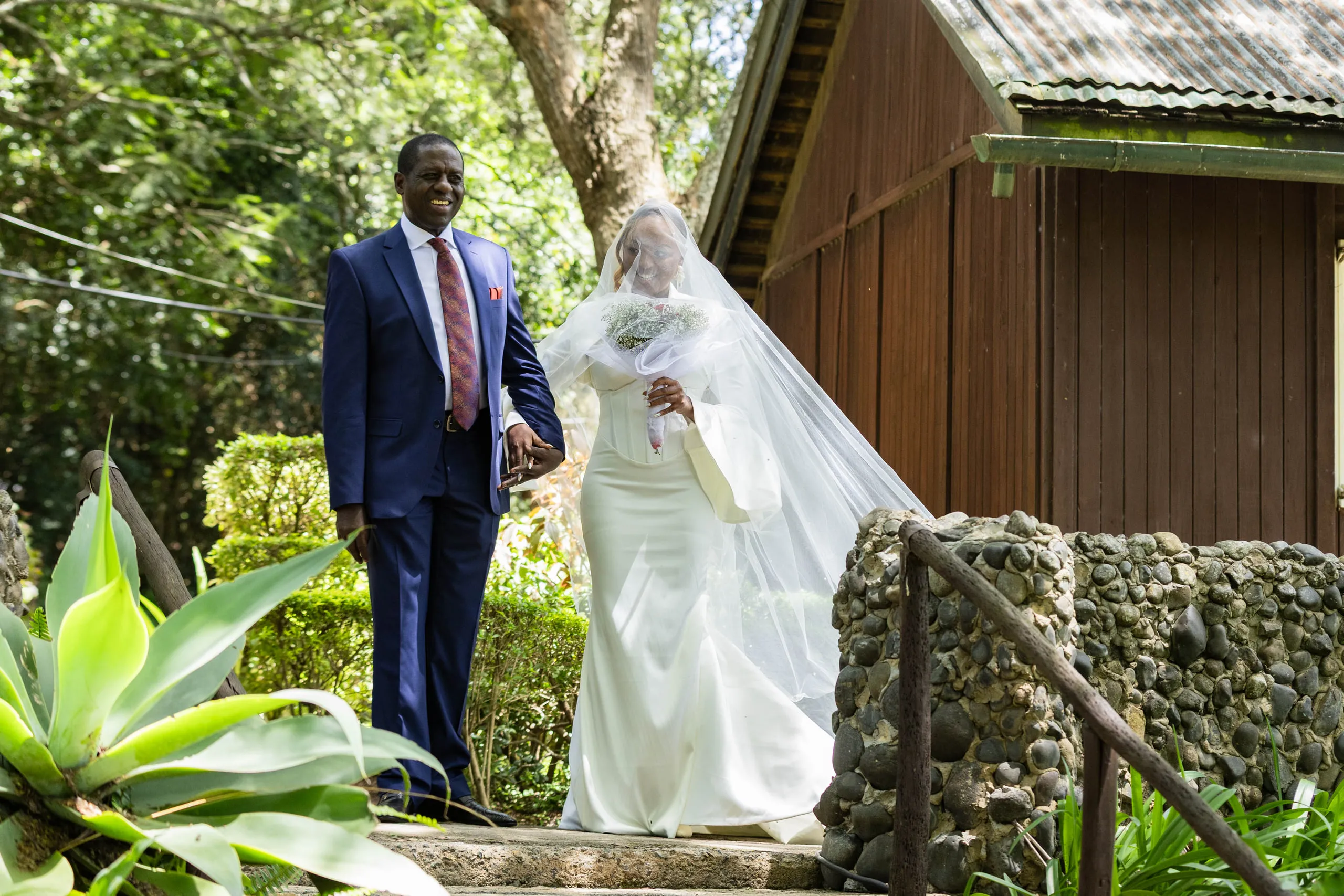 A man in a navy suit leading the veiled bride down the garden steps
