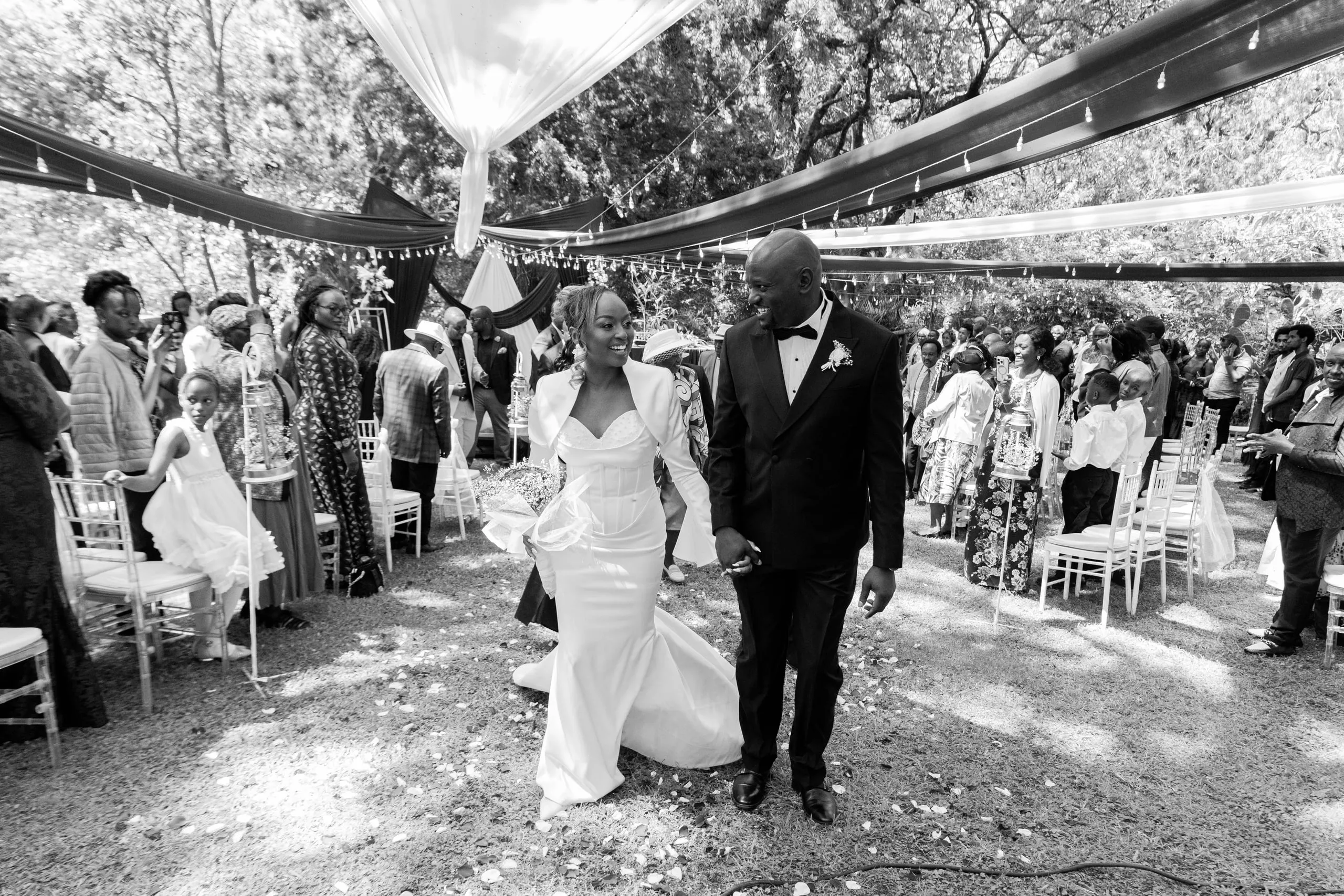 Bride and groom walking up the aisle between their guests, in black and white