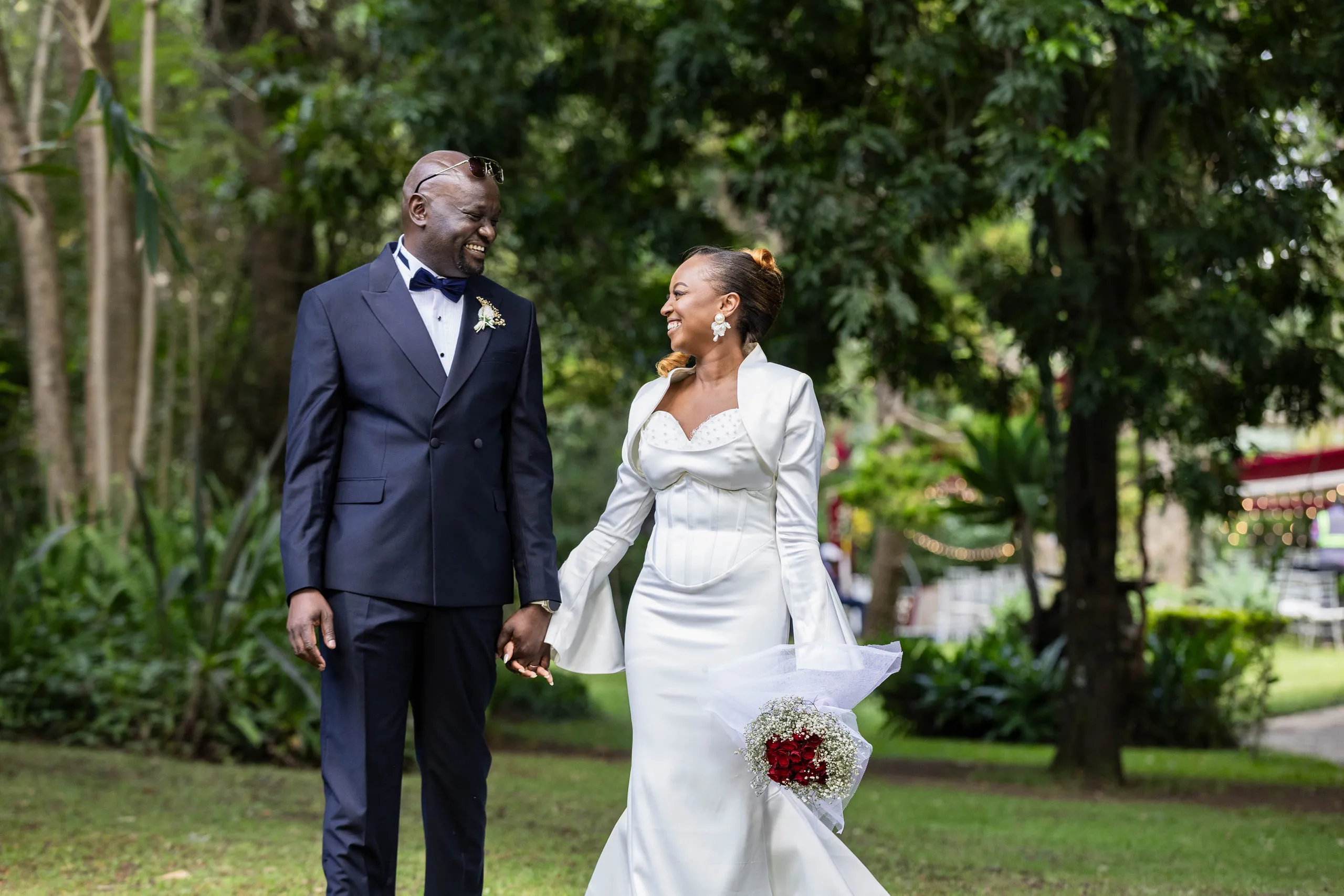 Bride and groom holding hands on a lawn, she carrying red roses