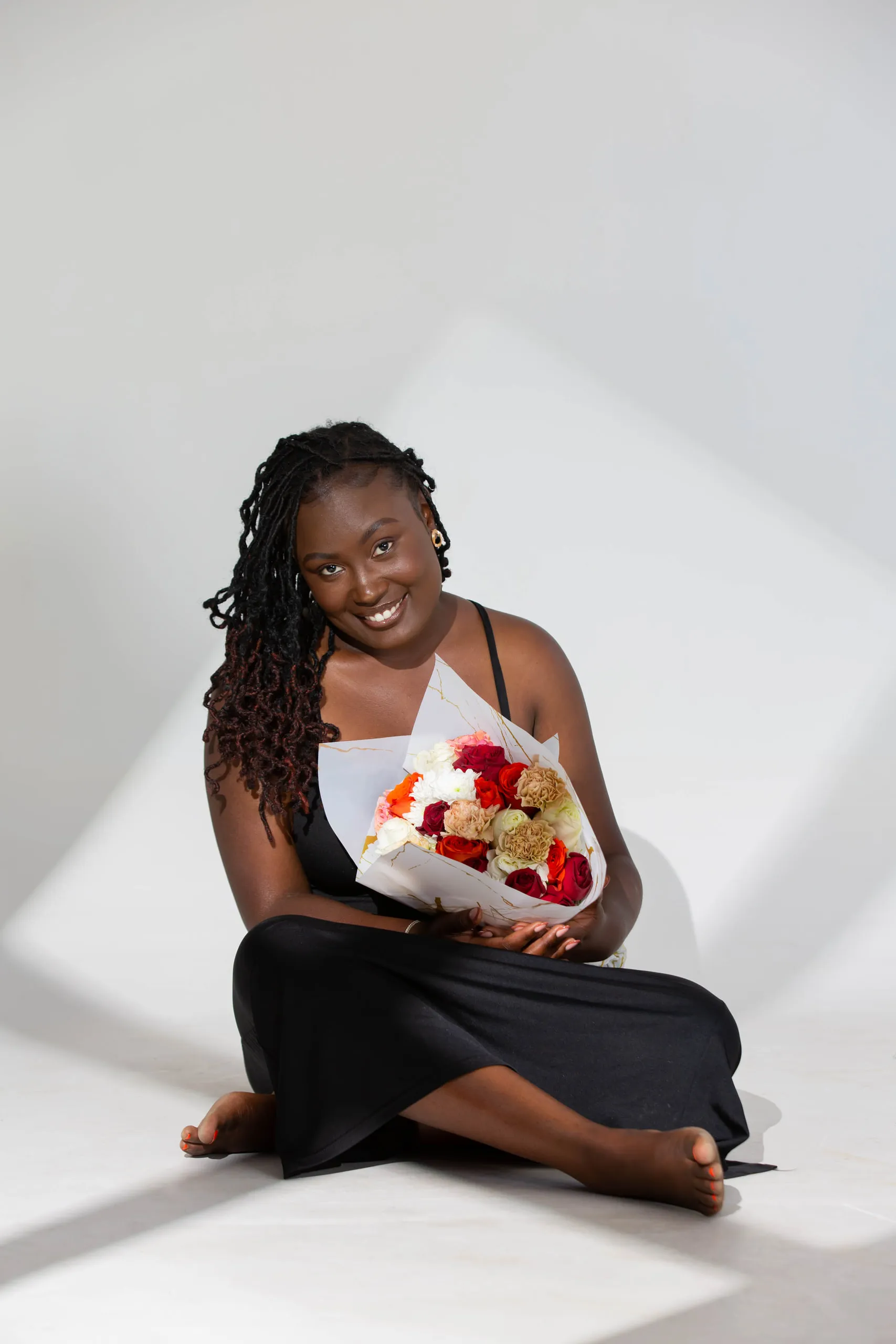 Woman in a black dress sitting on the floor holding a bouquet of red and white roses