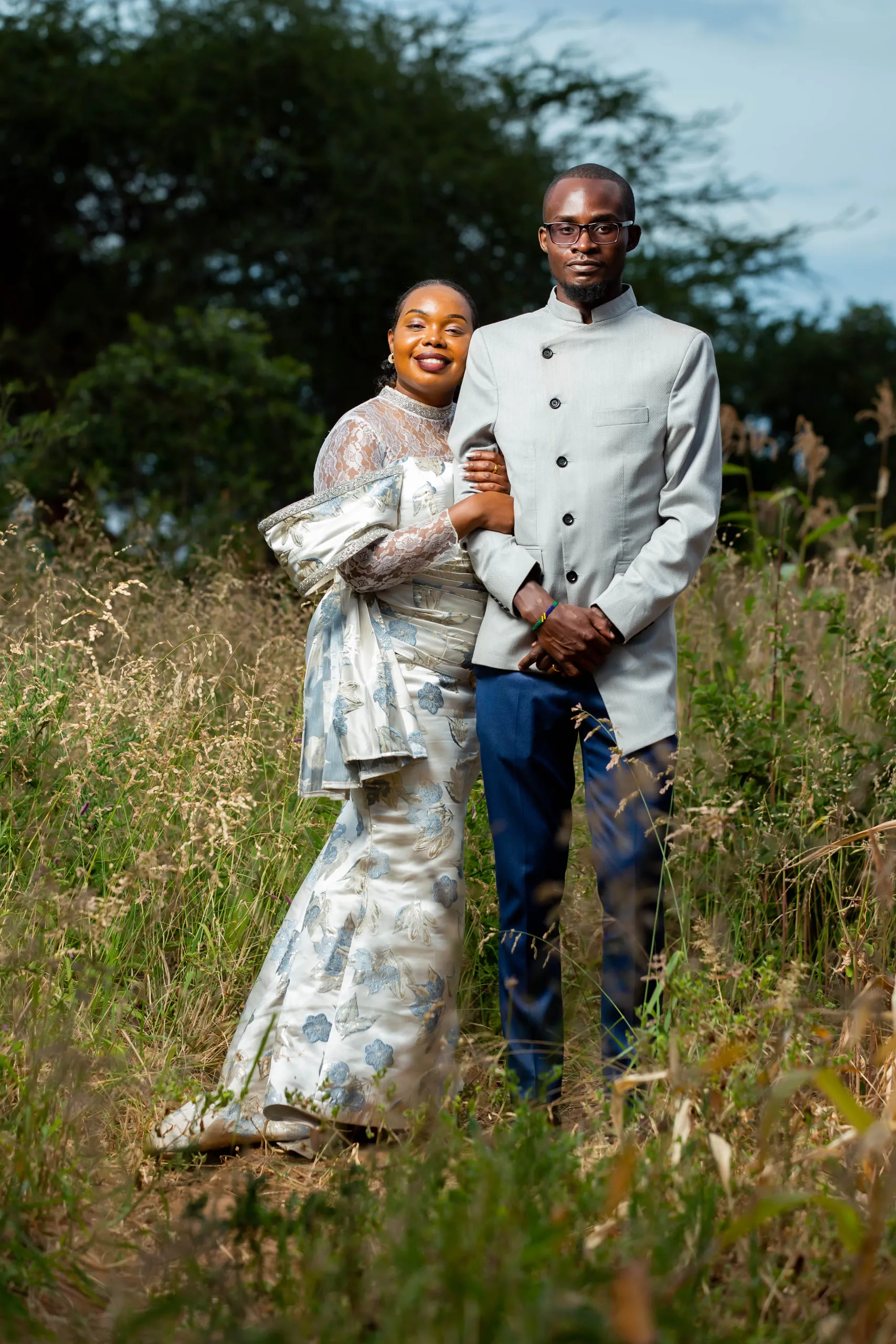 Couple standing in tall grass, he in a grey high-collared jacket
