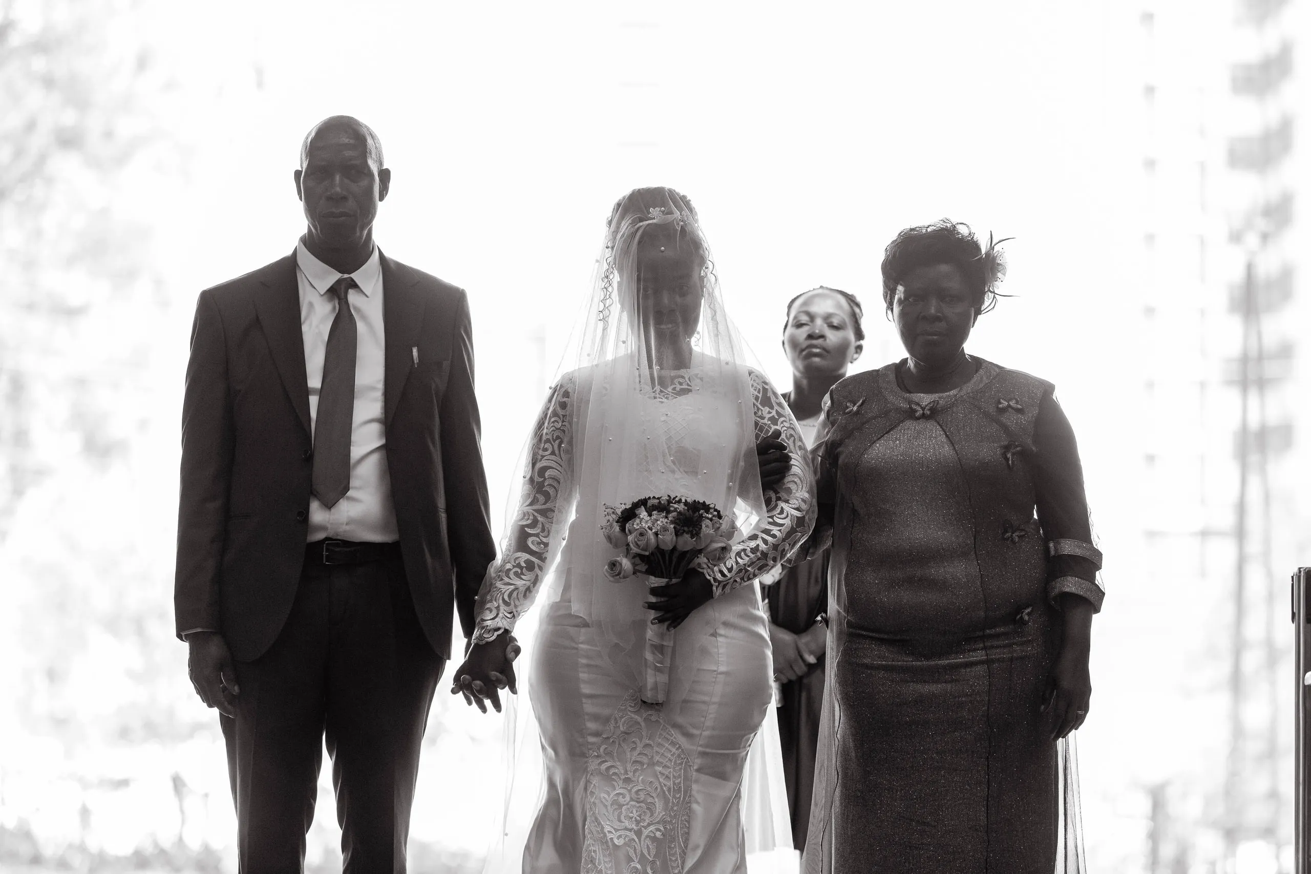 Veiled bride walking in between a man and a woman, in black and white