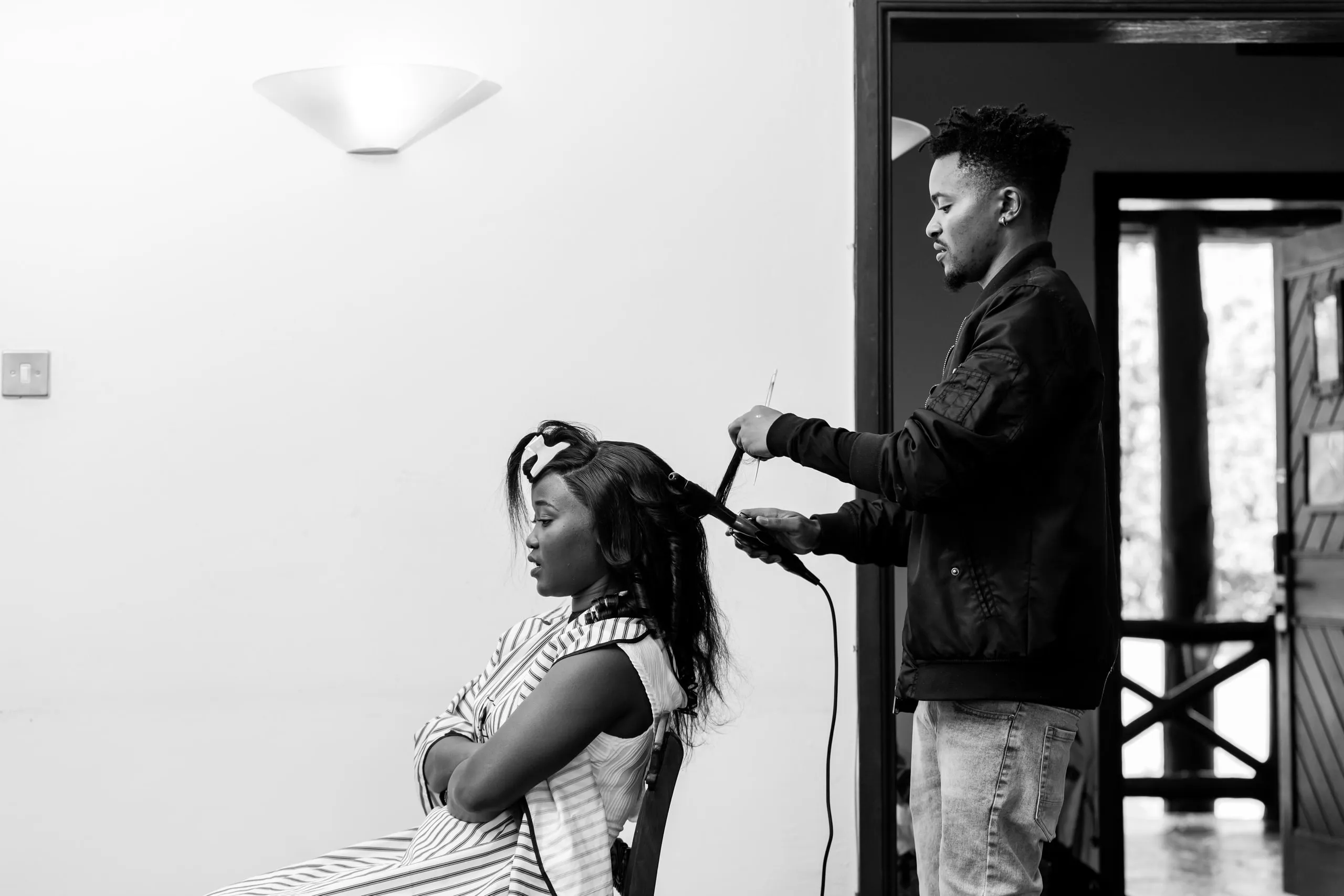 A stylist curling the bride's hair, in black and white
