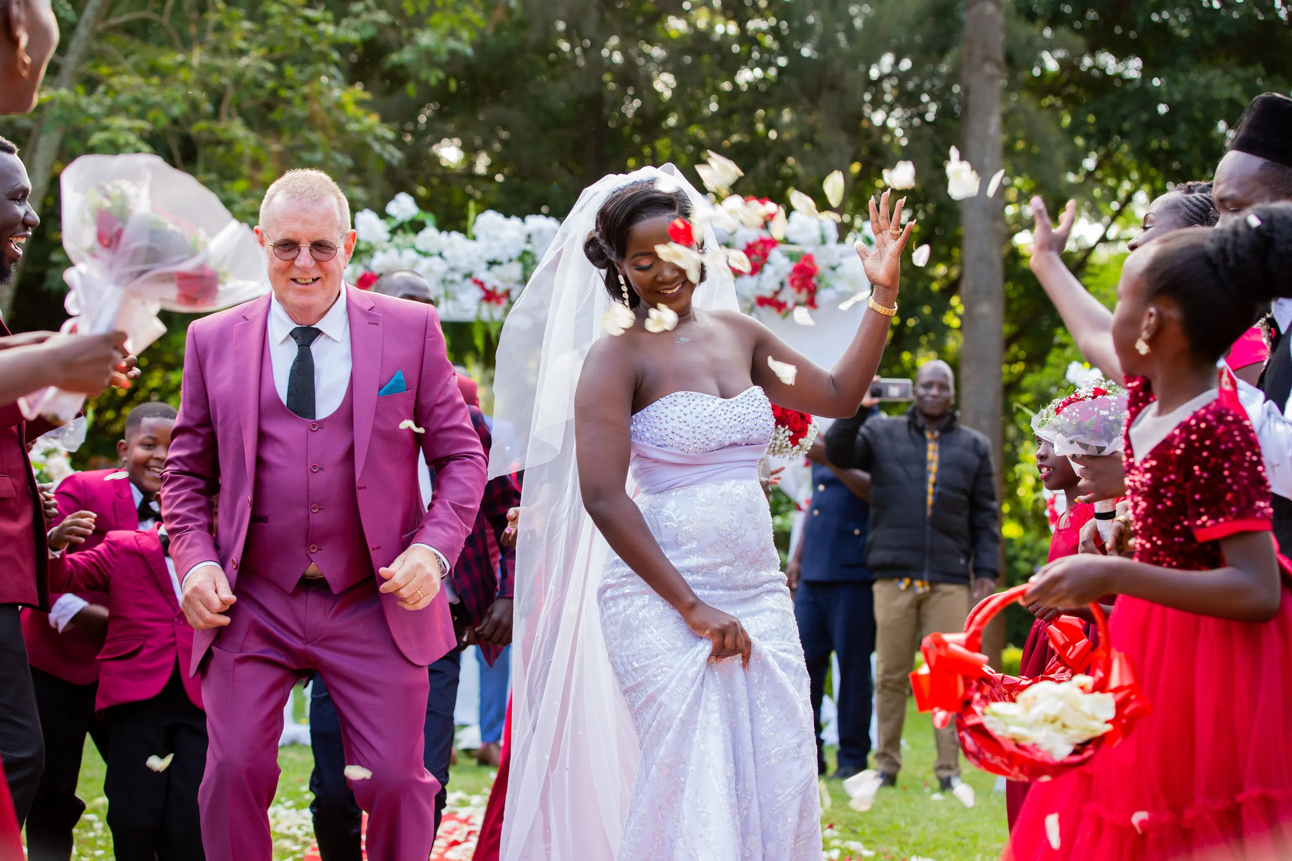 Bride and groom walking out under a shower of petals, flower girls in red