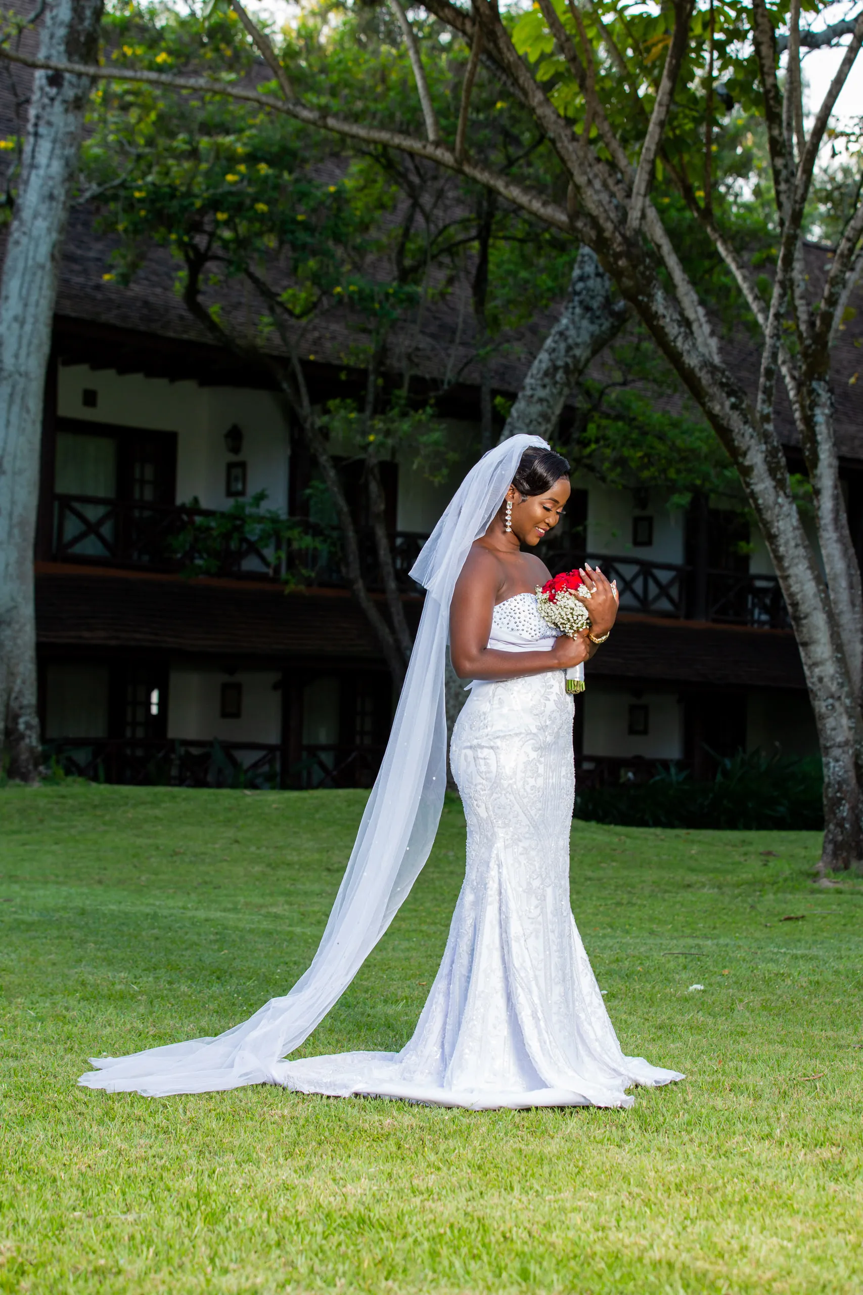 Bride with a long veil and red roses on a hotel lawn