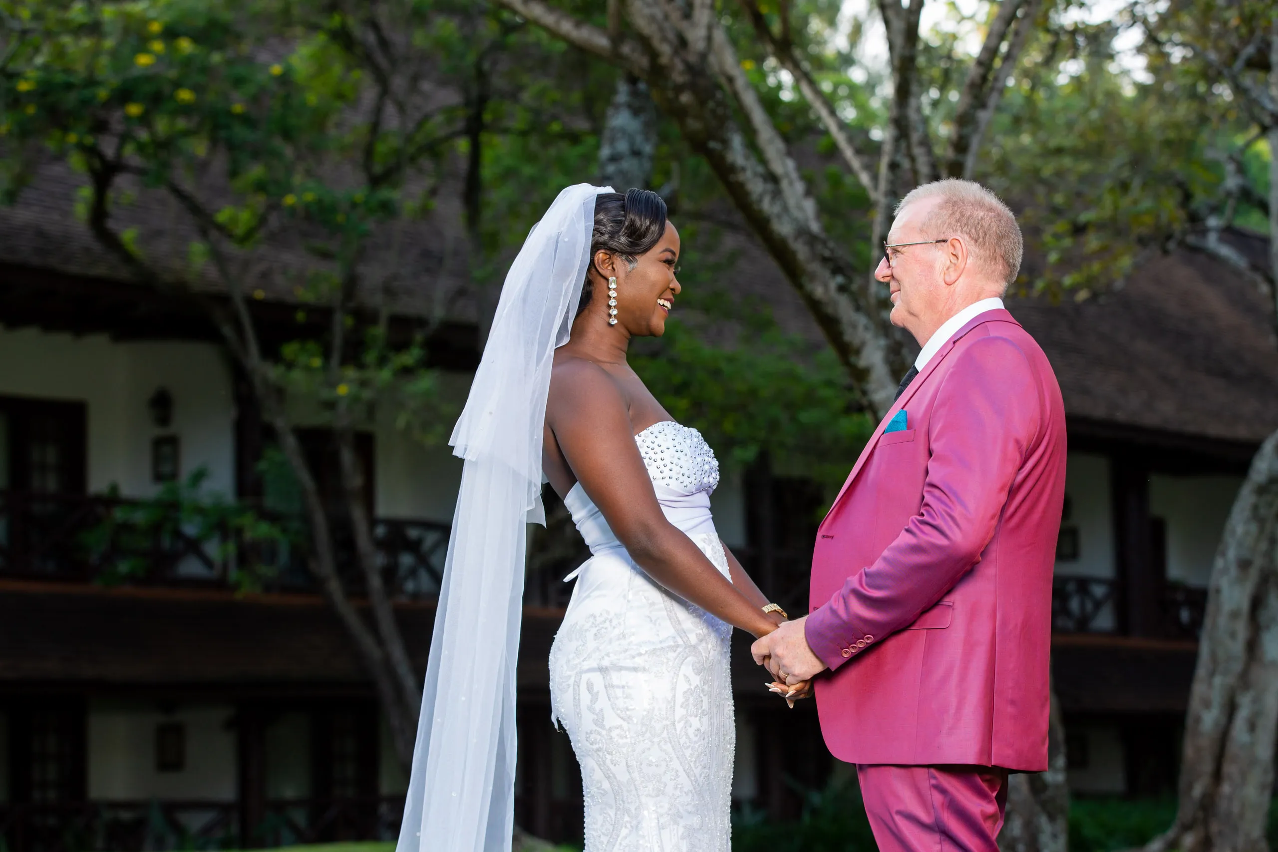 Bride and groom holding hands, he in a magenta suit