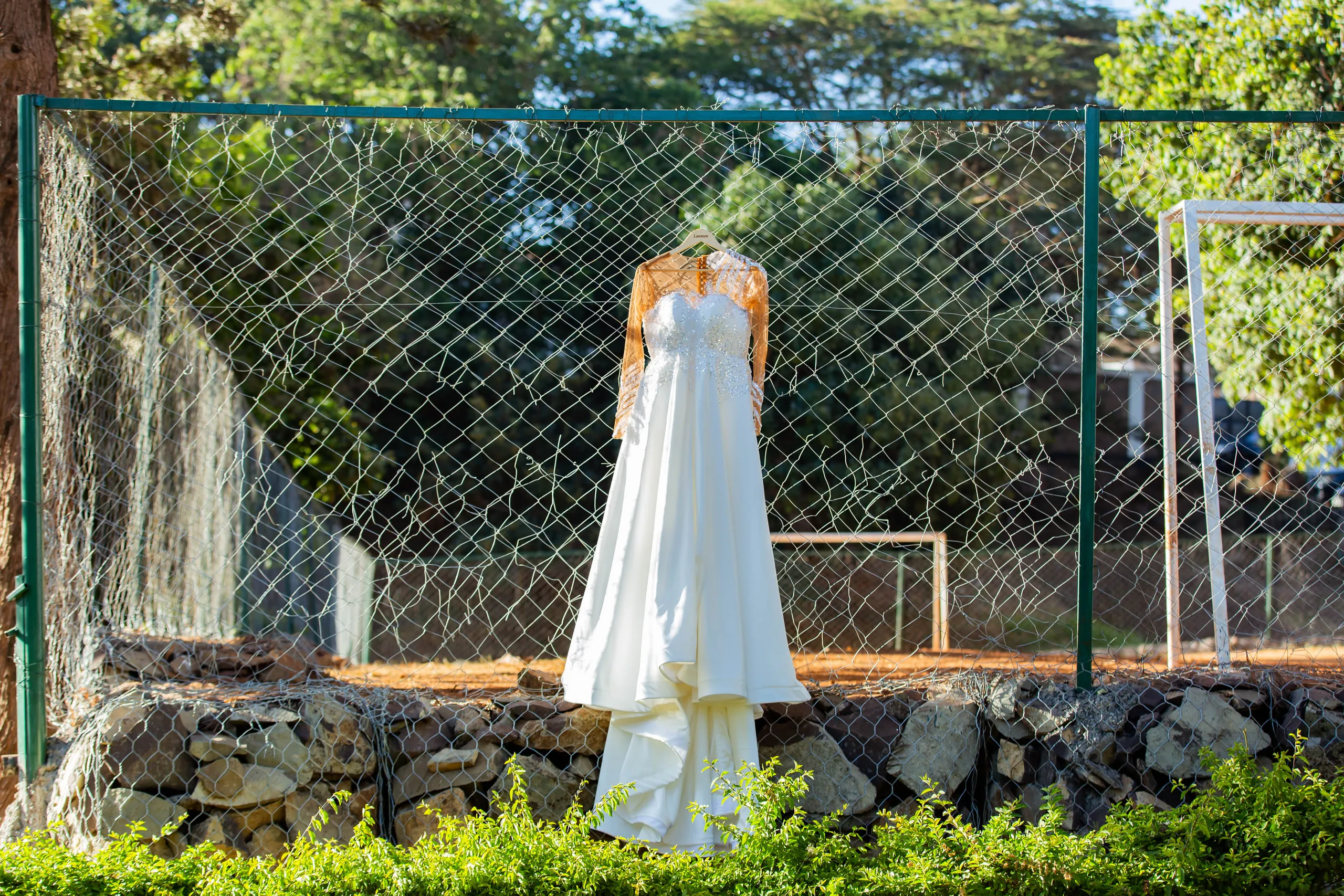 Wedding gown hanging on a fence beside a sports pitch