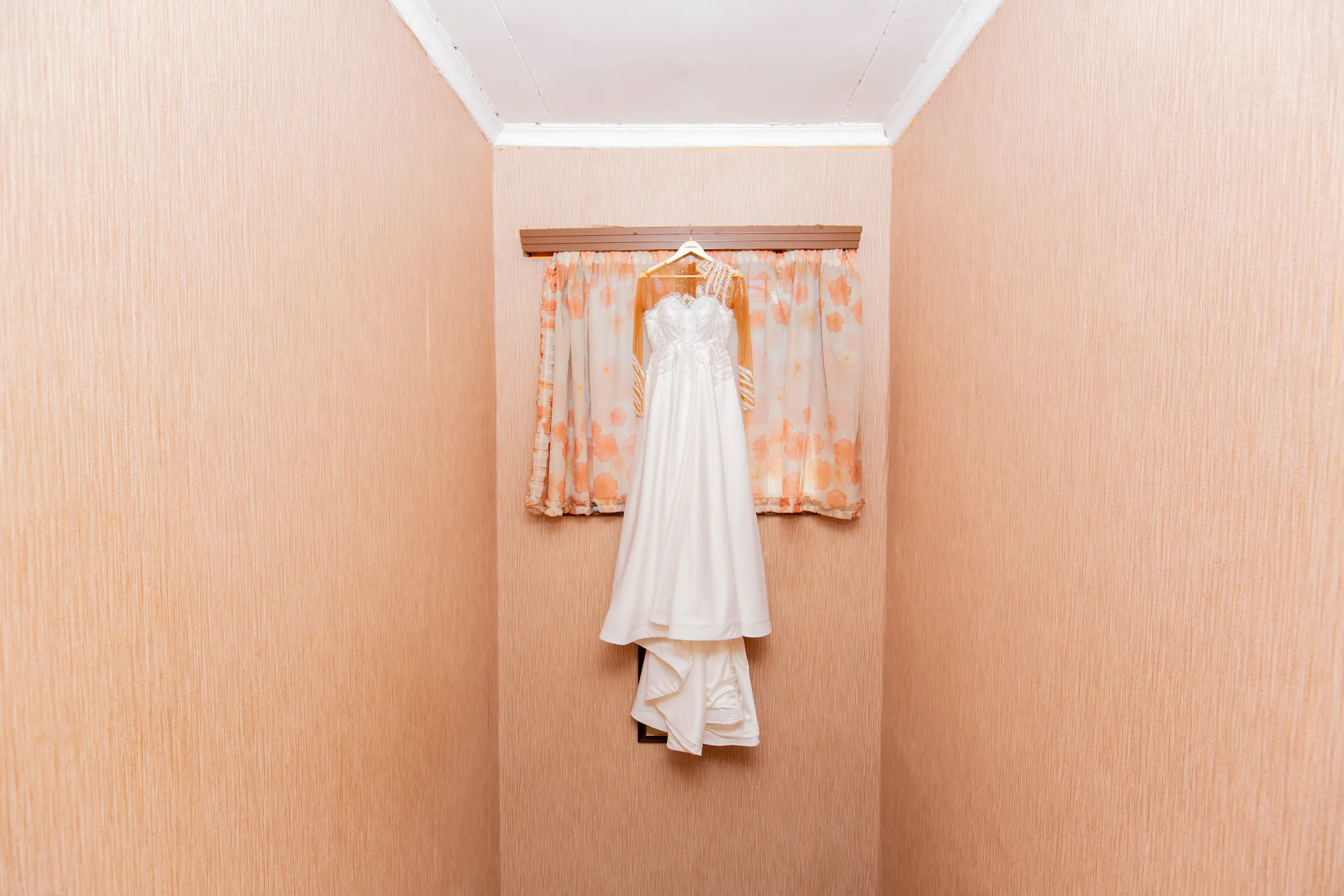 Wedding gown hanging on a peach wall