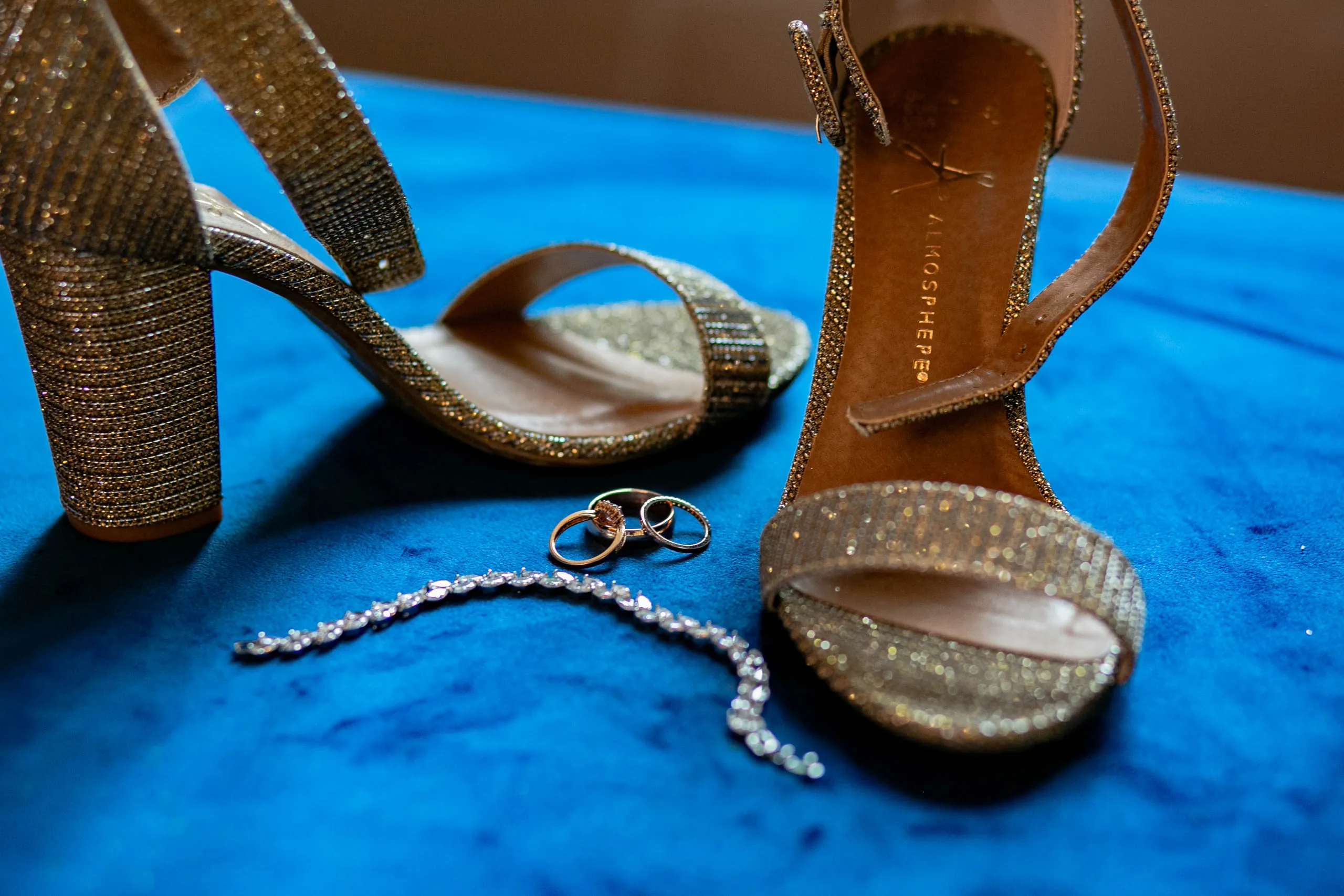 Glittering heels, wedding rings and a bracelet on blue velvet