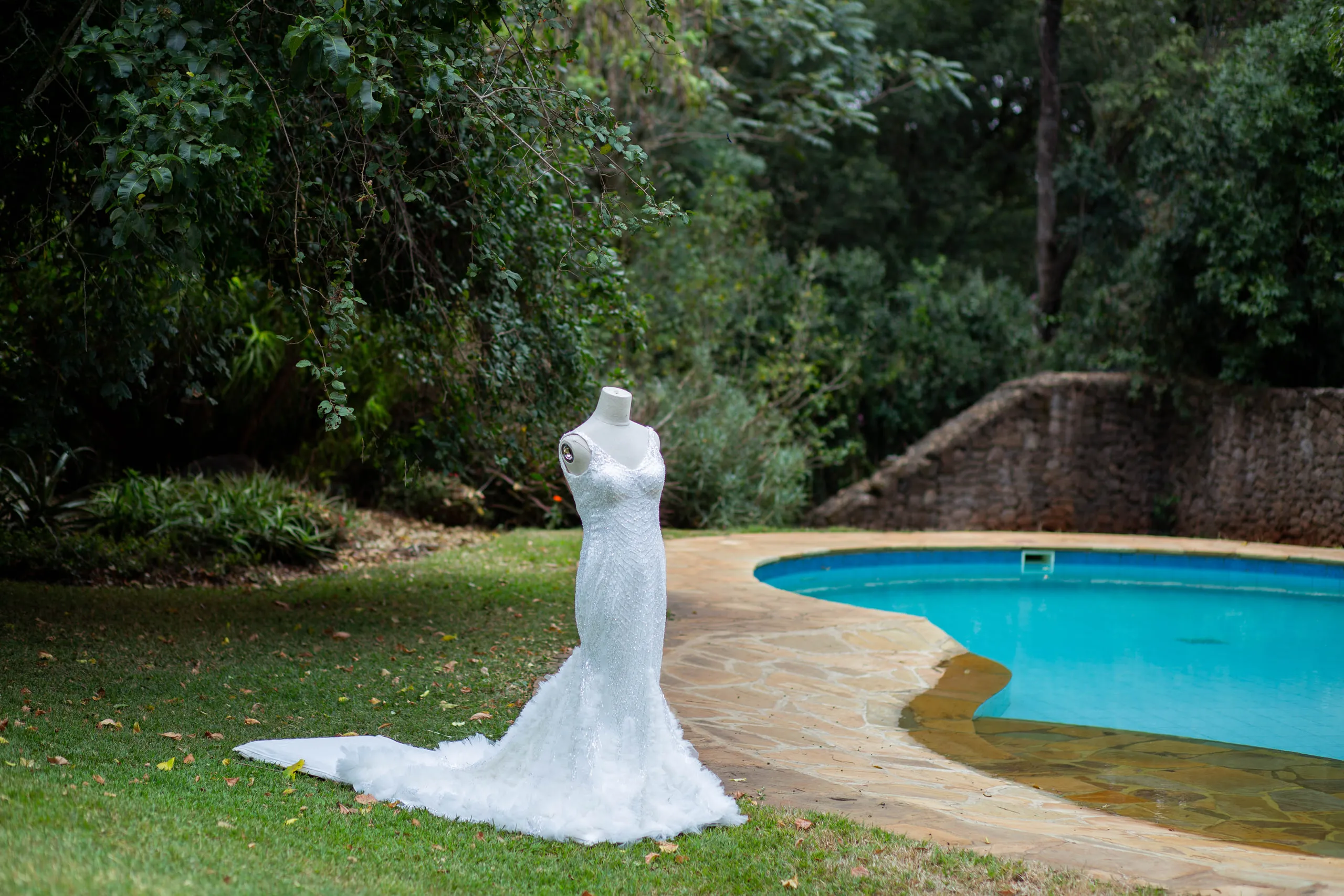 Wedding gown on a stand by the pool, framed by trees