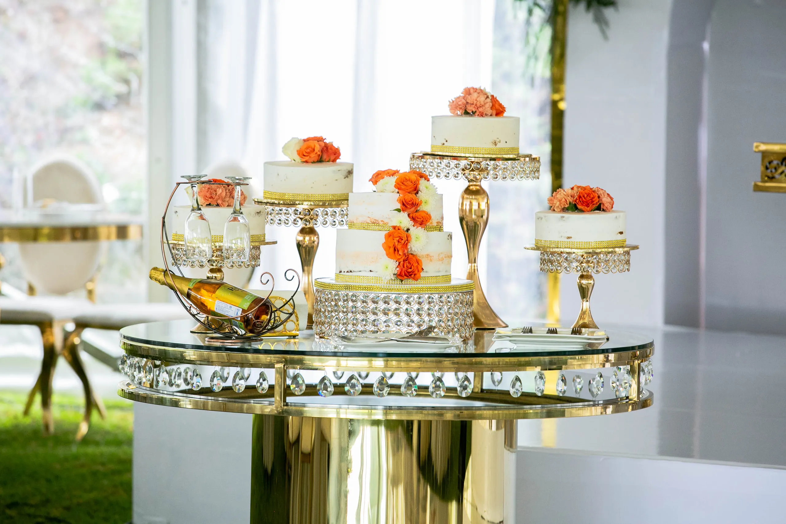 Small cakes topped with orange roses on a glass and gold table