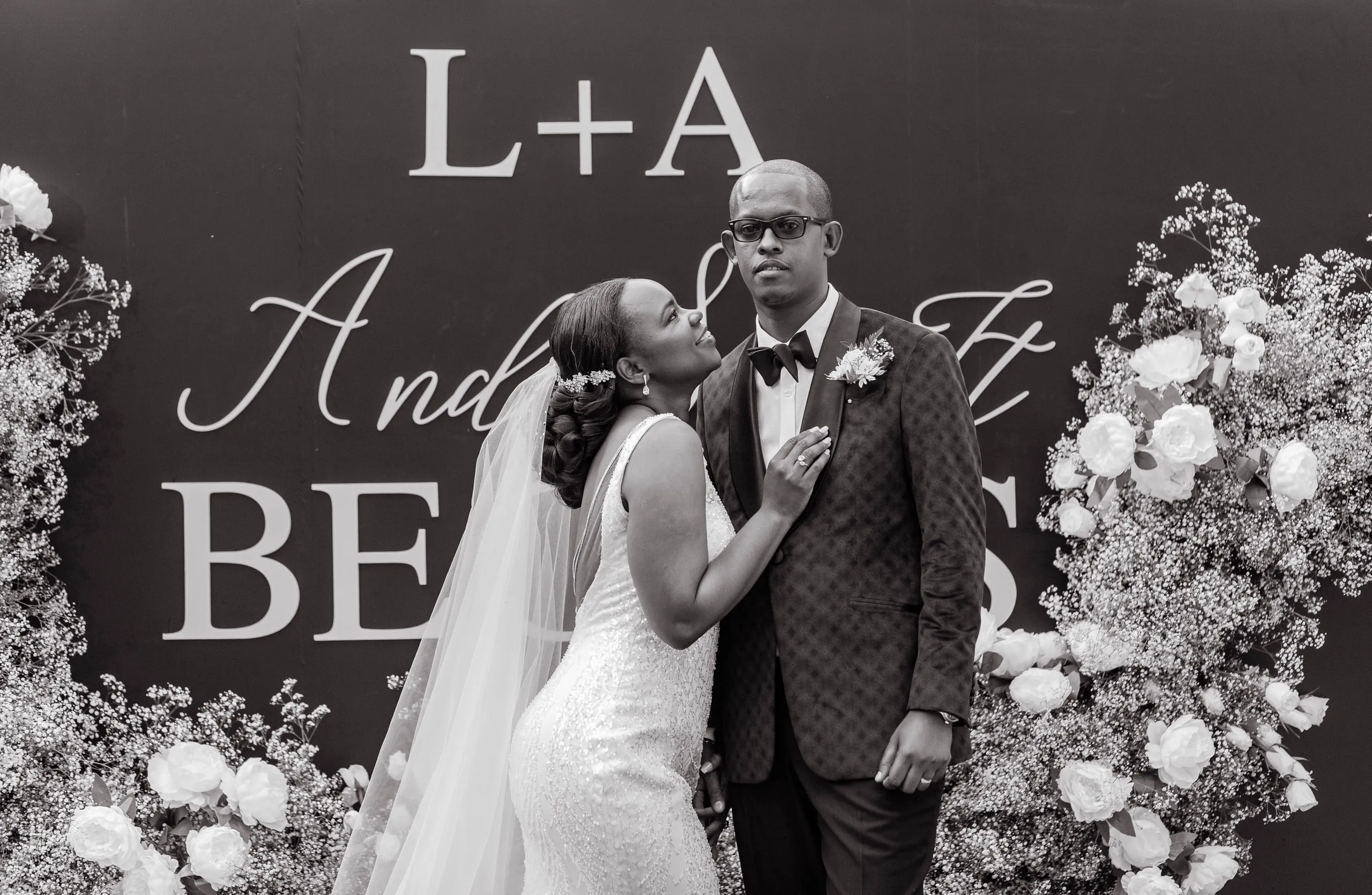 Bride and groom in front of a floral wall, in black and white