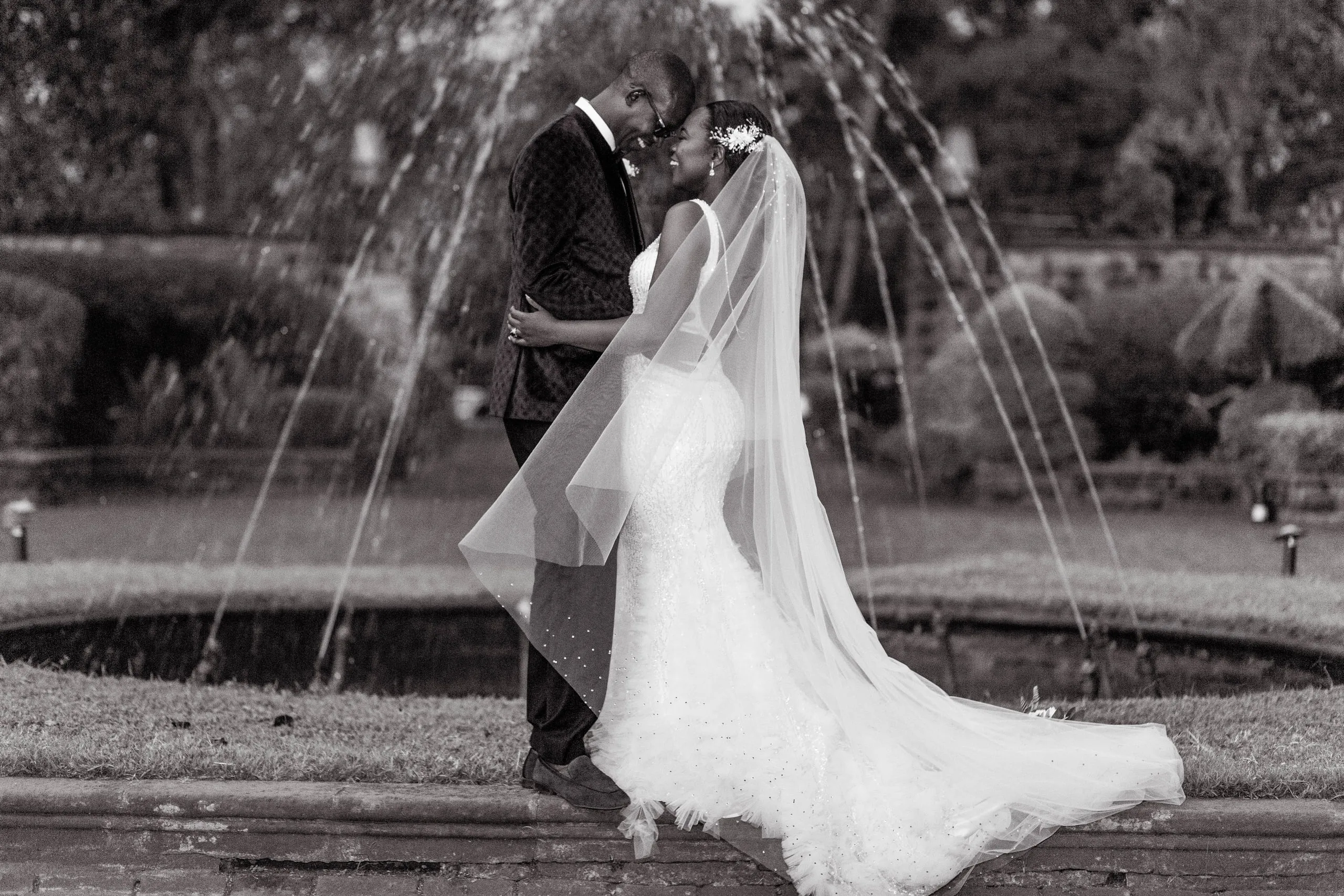 Bride and groom embracing beside a fountain, in black and white