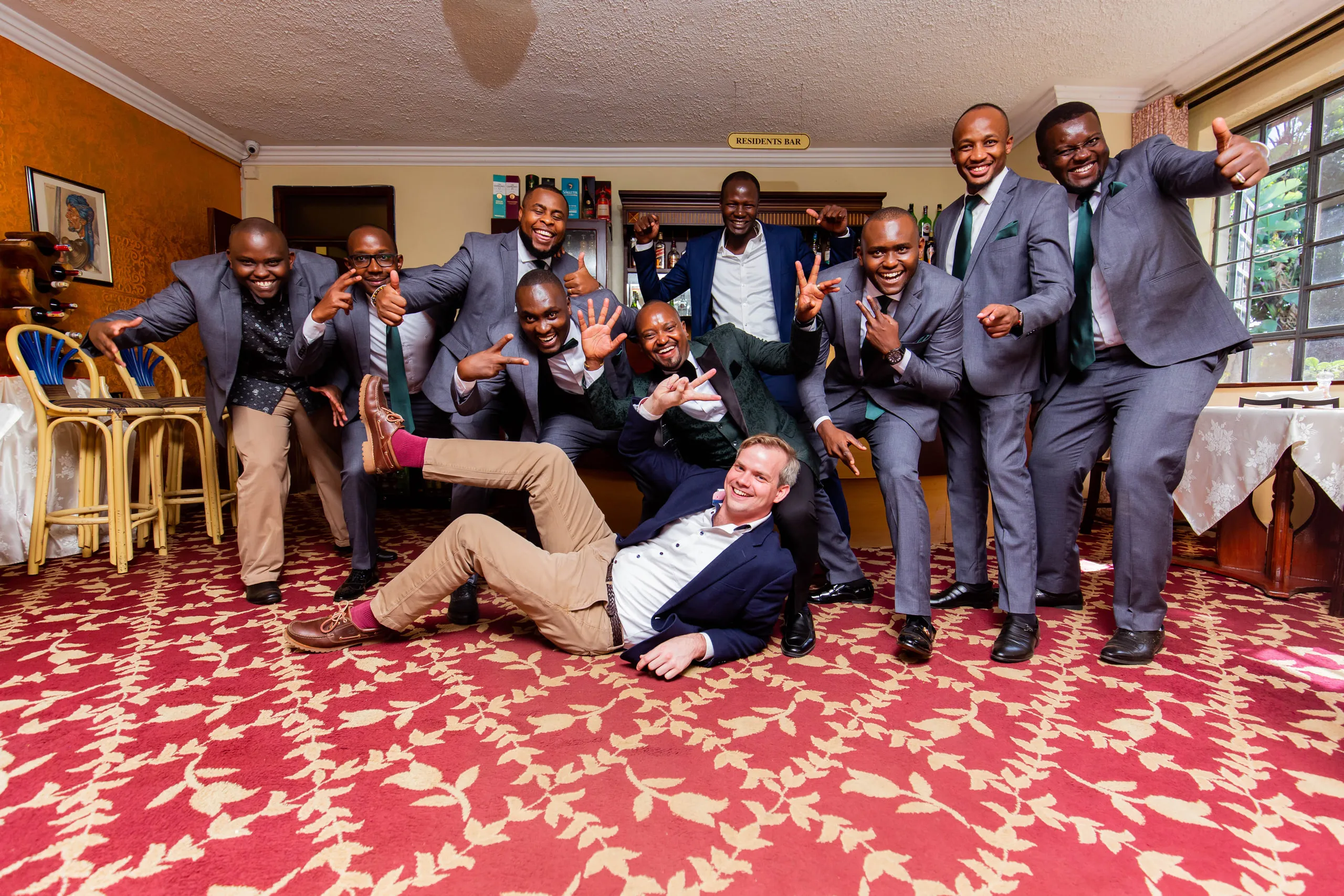 Groomsmen in grey suits clowning around, one lying on the carpet