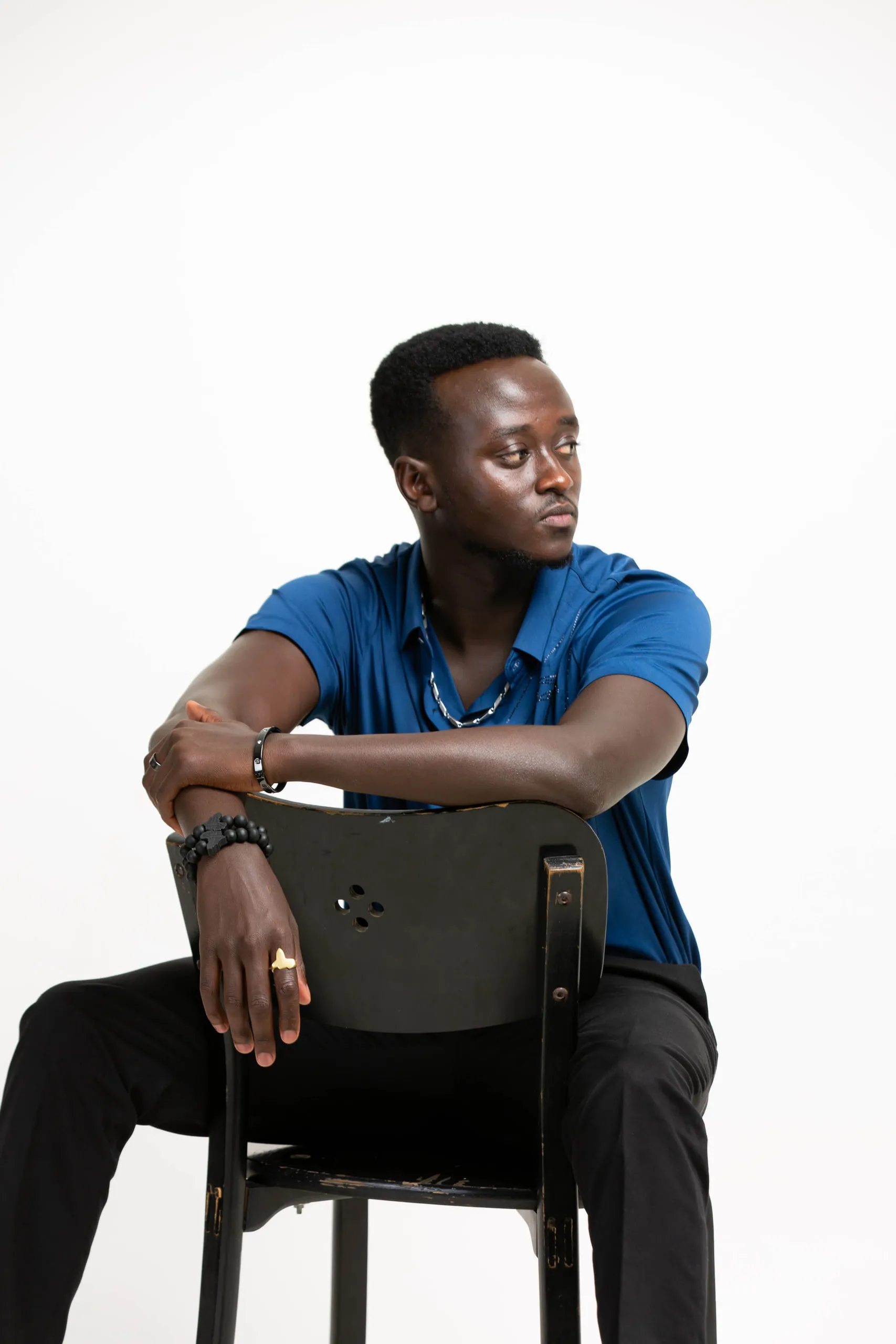 Man in a blue polo shirt sitting on a black chair with his arm on the backrest, looking away