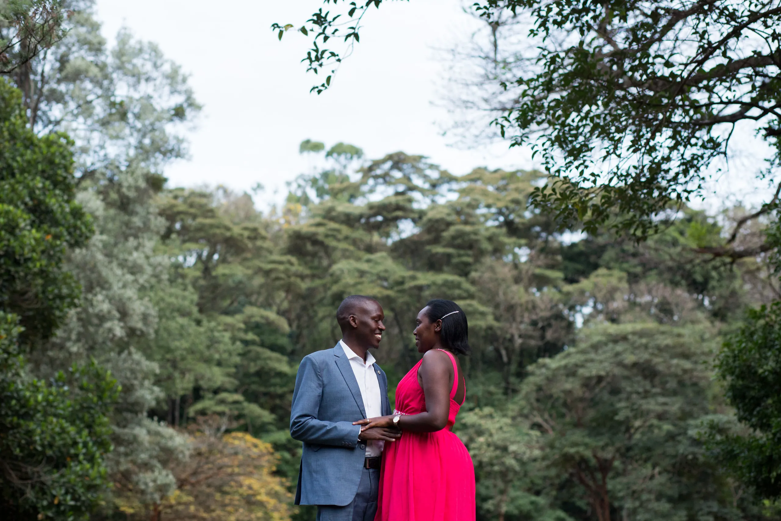 Couple facing each other among tall trees, she in pink, he in a blue suit