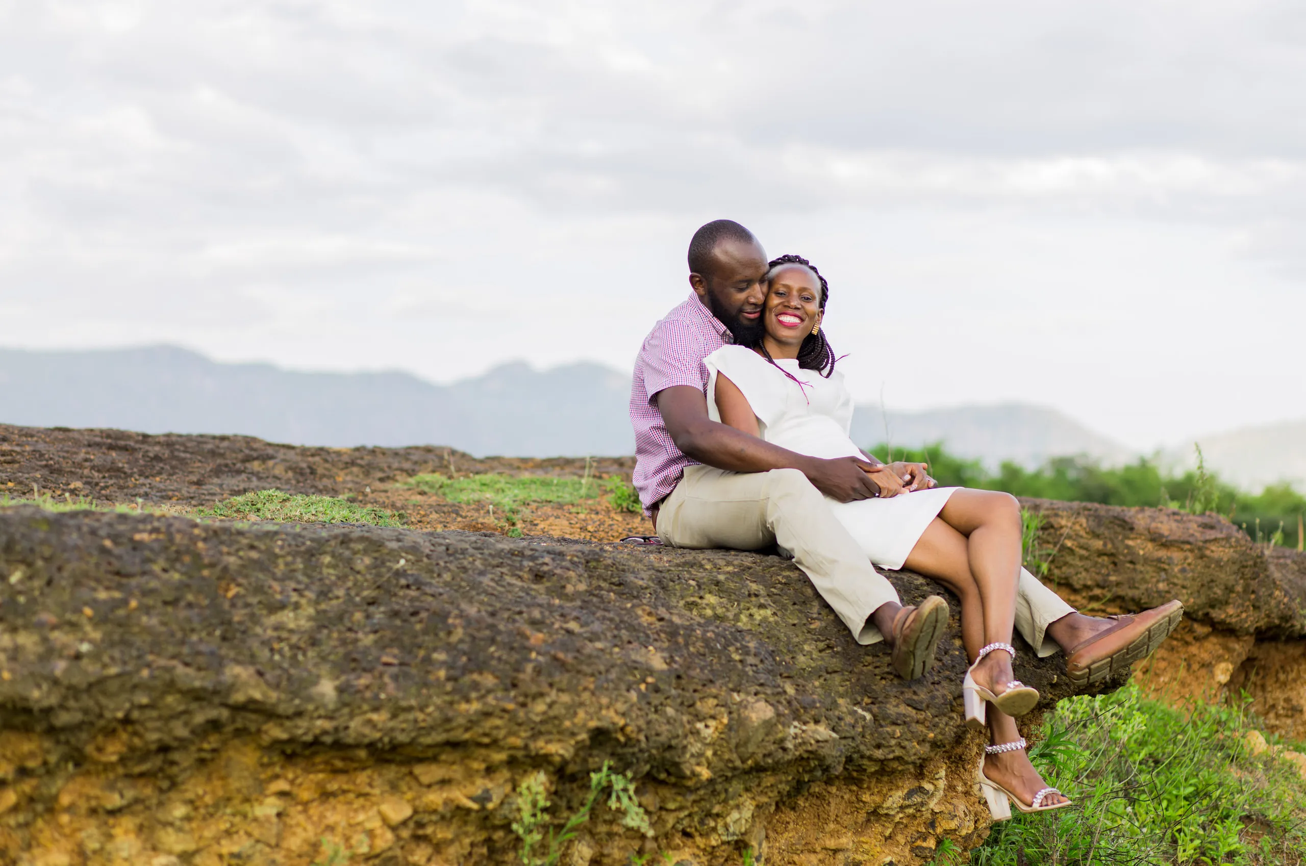 Couple sitting on a rocky ledge with hills behind them