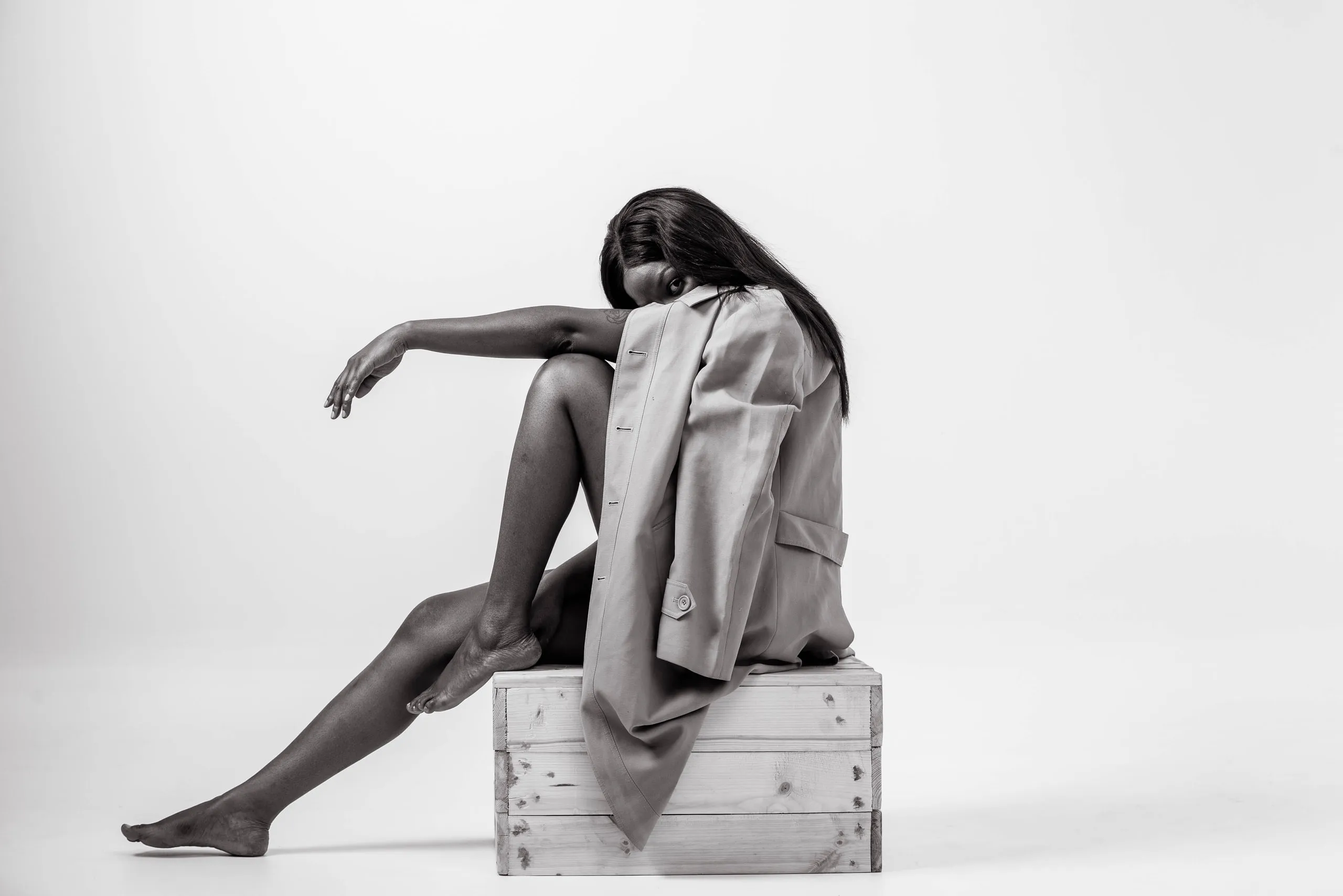 Woman seated on a wooden crate with a coat draped over her back, her head down, in black and white