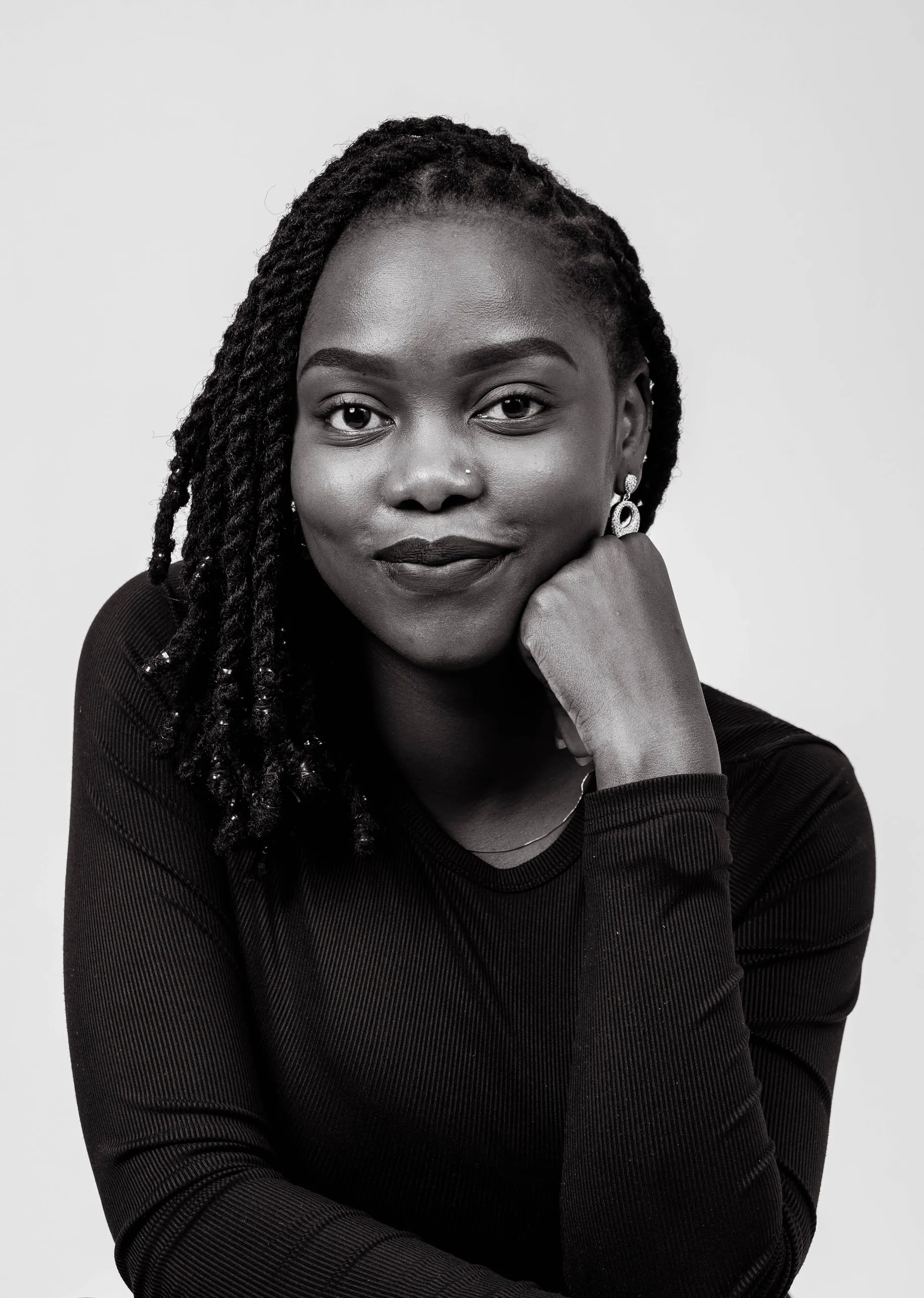 Woman with twisted locs resting her chin on her fist and smiling slightly, in black and white