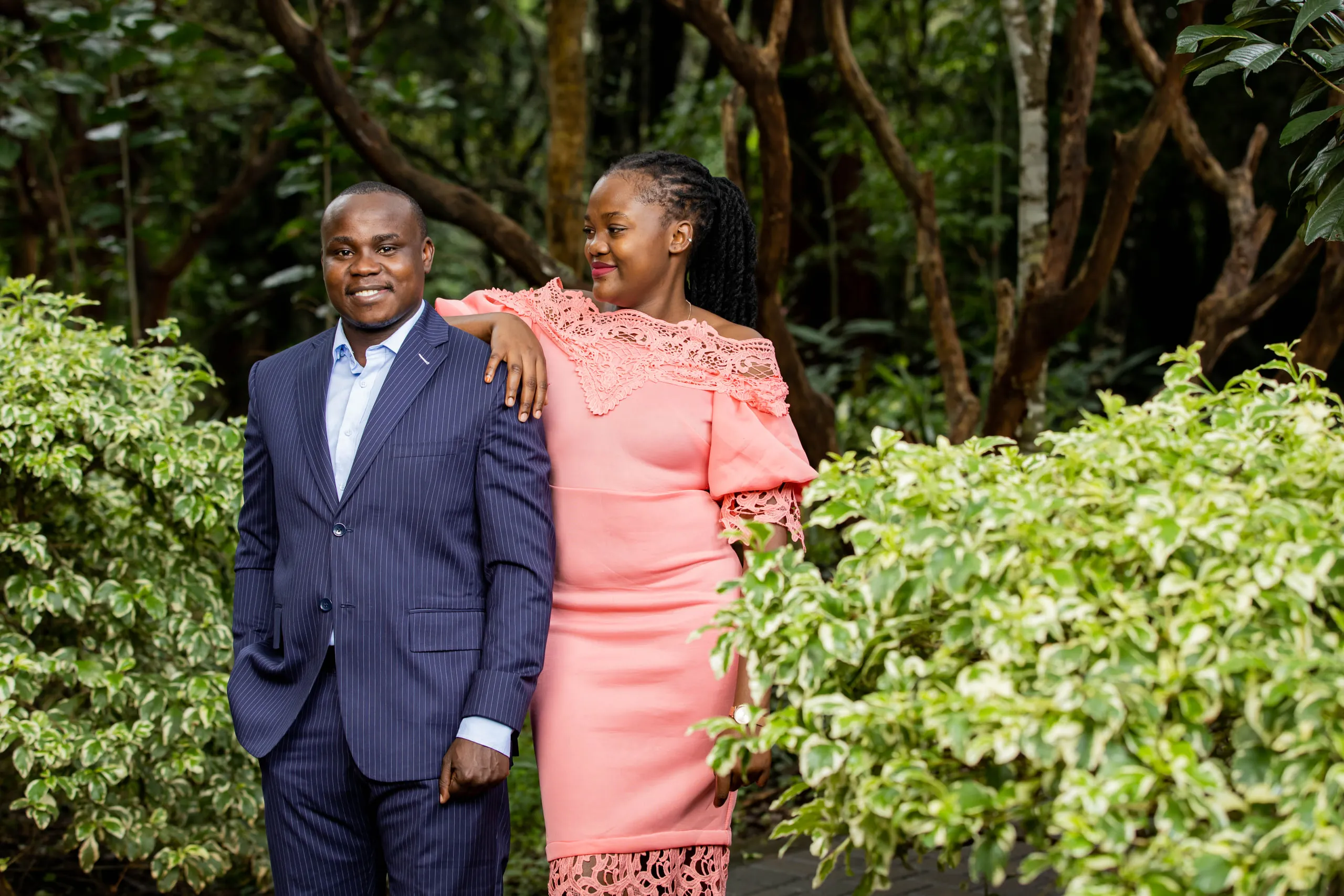 Couple between leafy bushes, her arm on his shoulder
